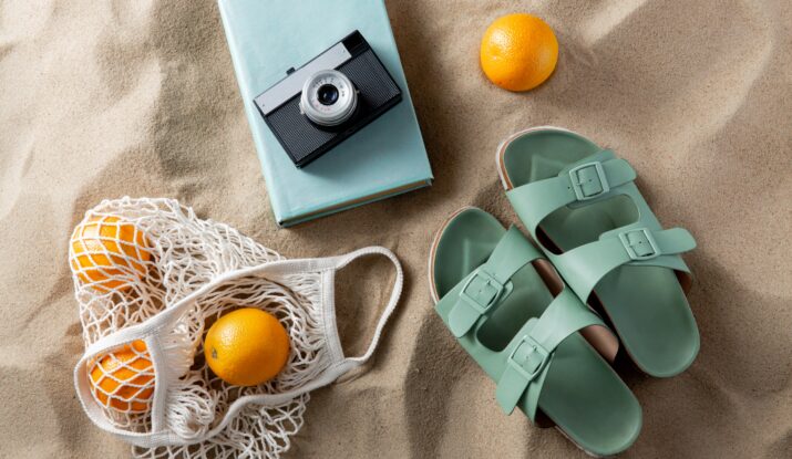 Summer essentials on sand: sandals, camera, oranges, book