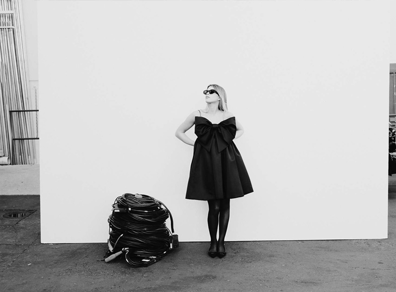 Woman in black bow dress against white wall