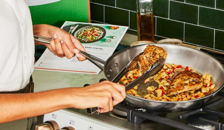 Person cooking seasoned chicken breast in skillet