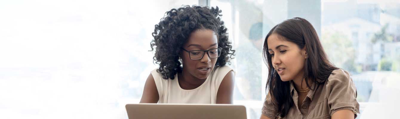 Two women collaborating over laptop in bright office