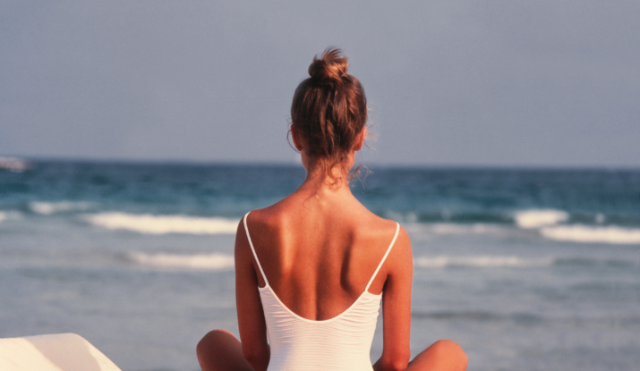 Woman sitting on beach chair facing ocean waves