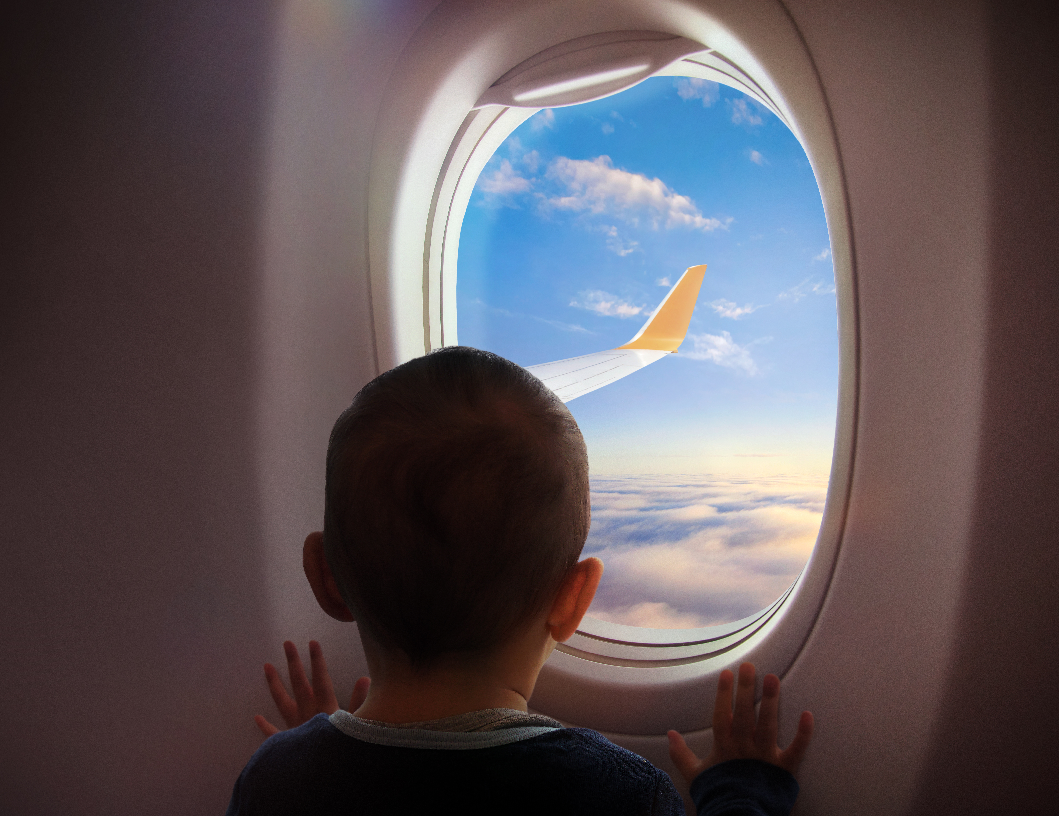 Child looking out airplane window at wing and clouds
