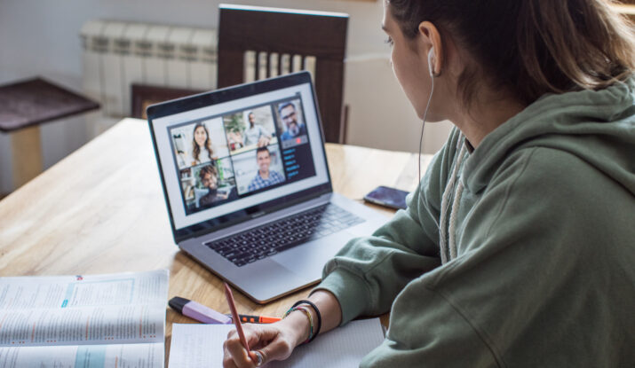 Person attending online meeting while taking notes
