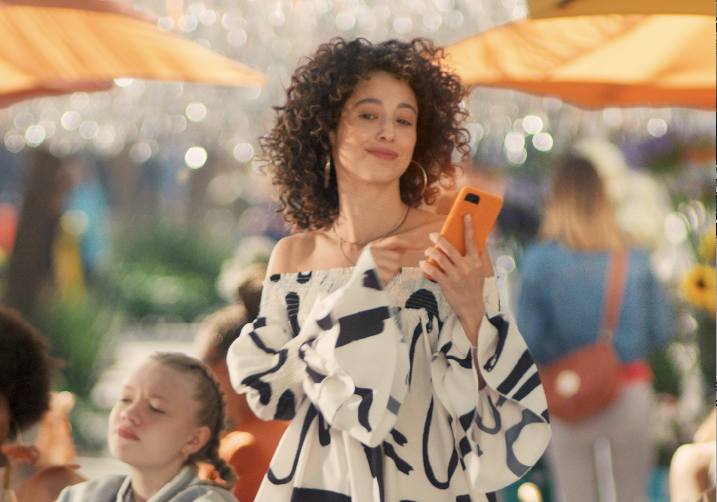 Curly-haired woman using orange phone outdoors