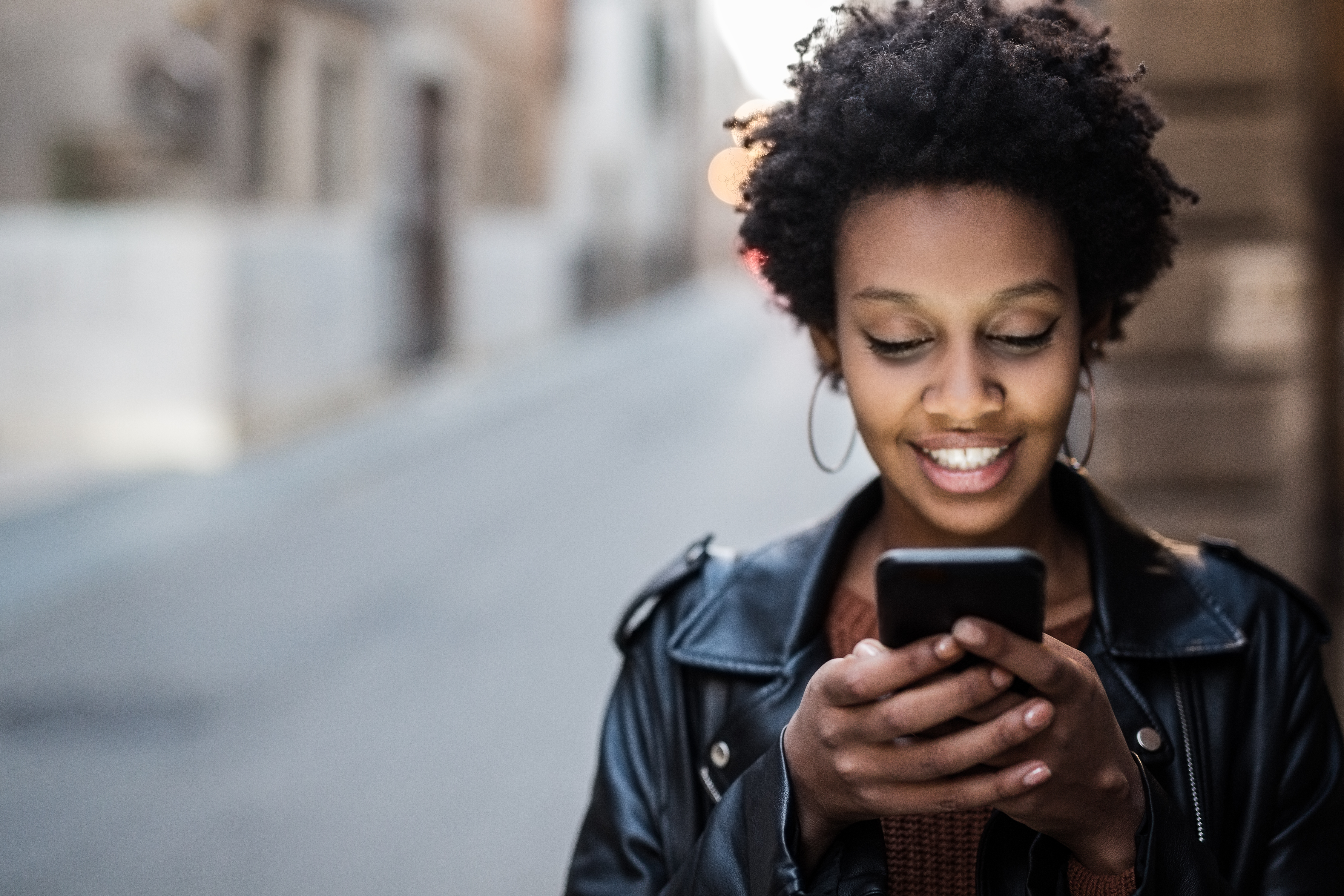 Woman smiling while using smartphone outdoors