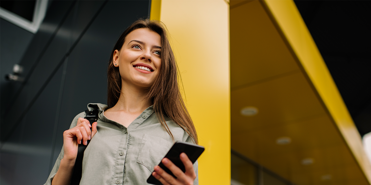 Smiling woman holding phone near yellow building