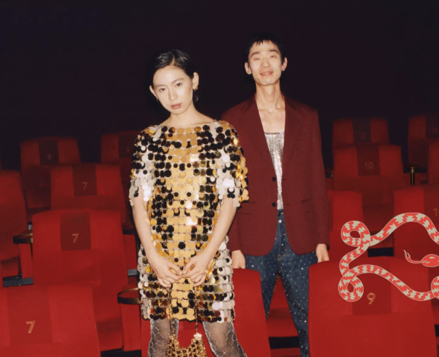 Two fashionably dressed people standing among red theater seats
