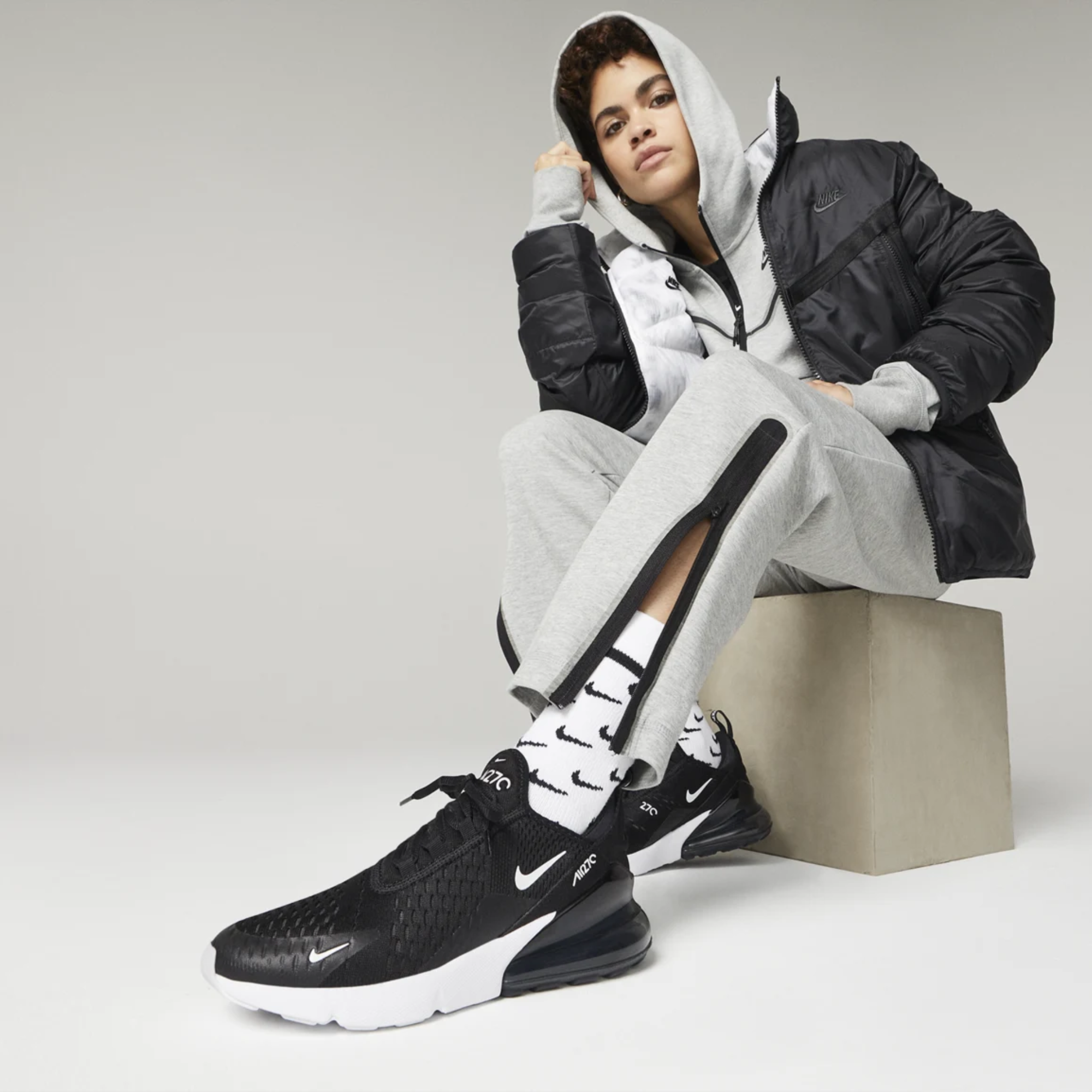 Person seated wearing black Nike sneakers and gray tracksuit