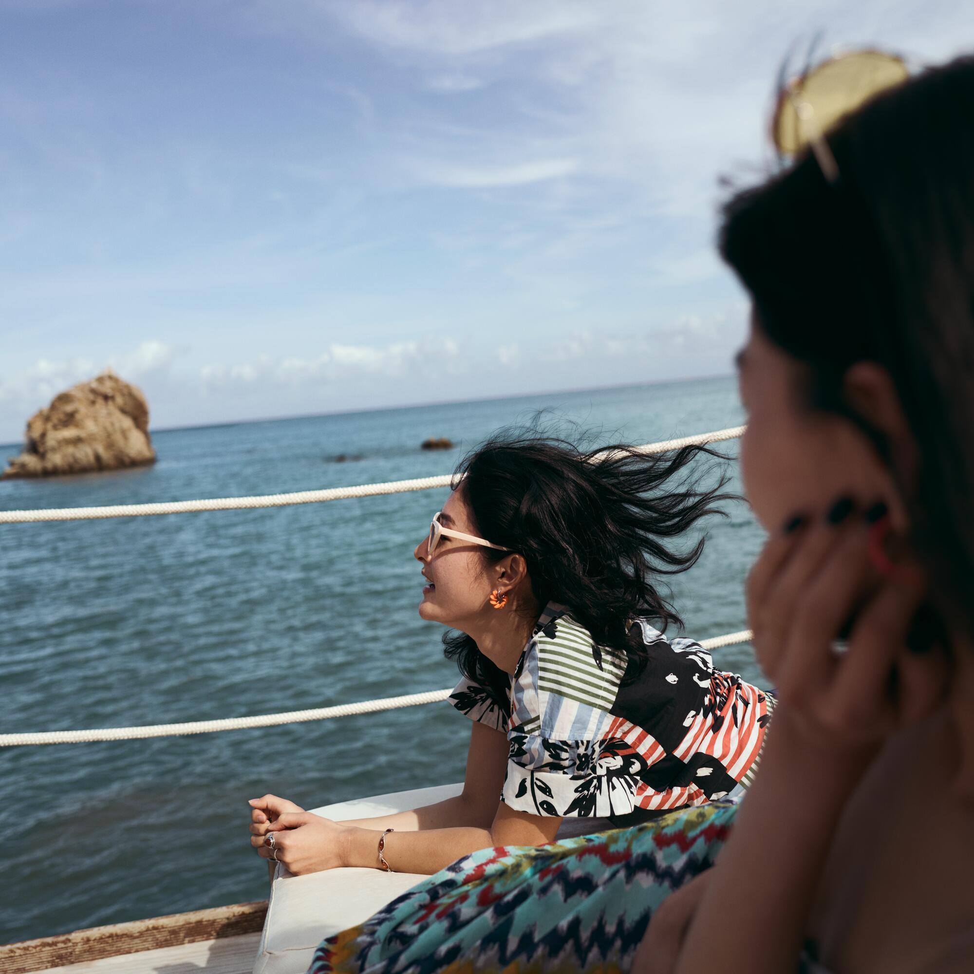 Woman leaning on railing looking at sea with wind blowing hair